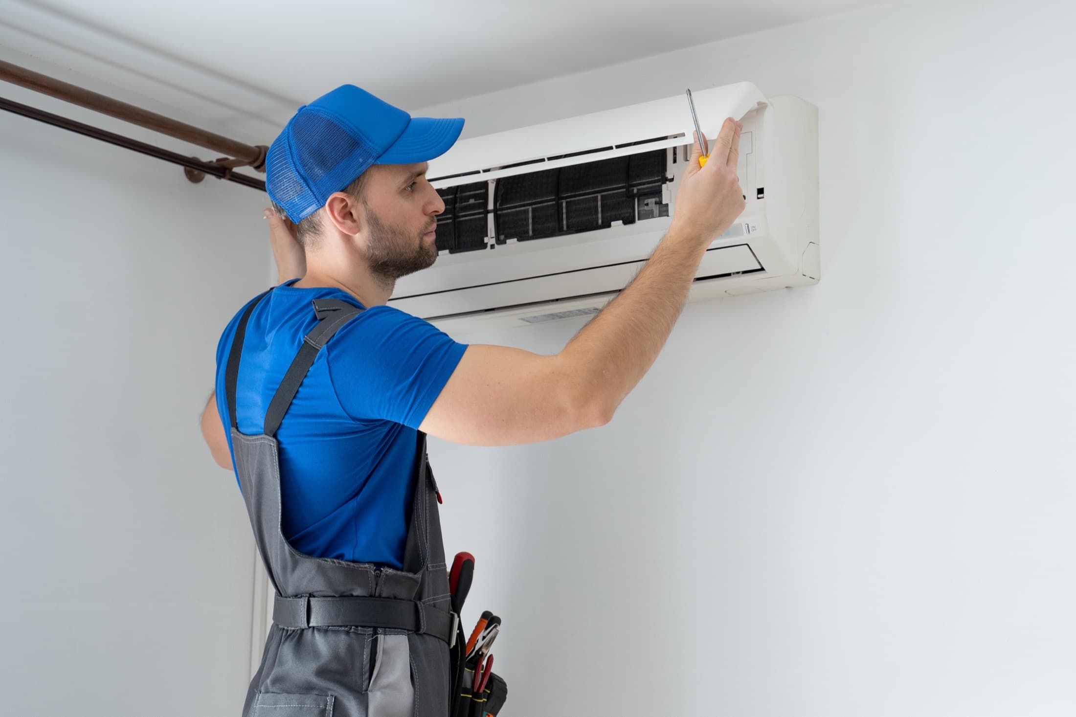 HVAC technician in overalls repairing an air conditioner mounted on a wall